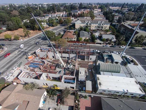 Aerial view of a construction site beside a busy intersection, with cranes and partially built structures.