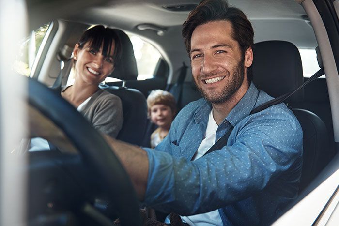 Two smiling adults and a child sitting in a car, seen from the front seat