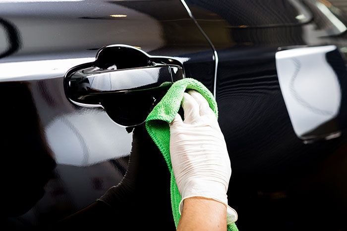 Gloved hand wiping a black car door with a green cloth