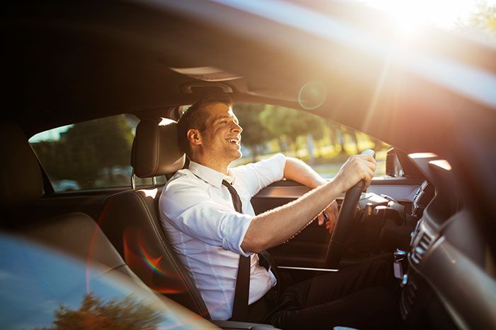 Driver at the wheel of a car, smiling in warm sunlight with lens flare through the windshield