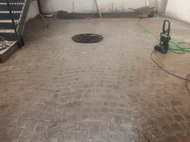 Suelo de hormigón mojado con un desagüe en el centro y una hidrolavadora a la derecha