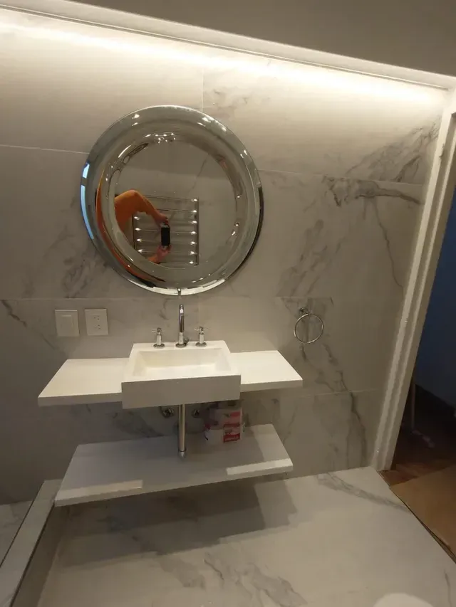 Mueble de baño moderno con espejo redondo, lavabo blanco y azulejos de mármol en las paredes y el suelo