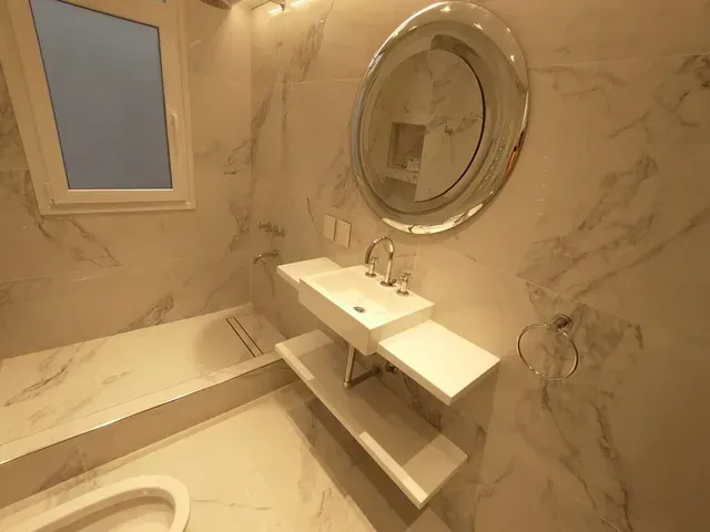 Baño moderno de mármol con bañera, lavabo suspendido, espejo redondo y ventana