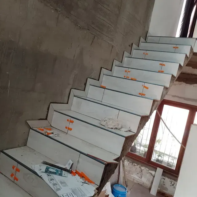 Escalera de hormigón sin terminar en construcción dentro de un edificio, con peldaños blancos y marcas naranjas.