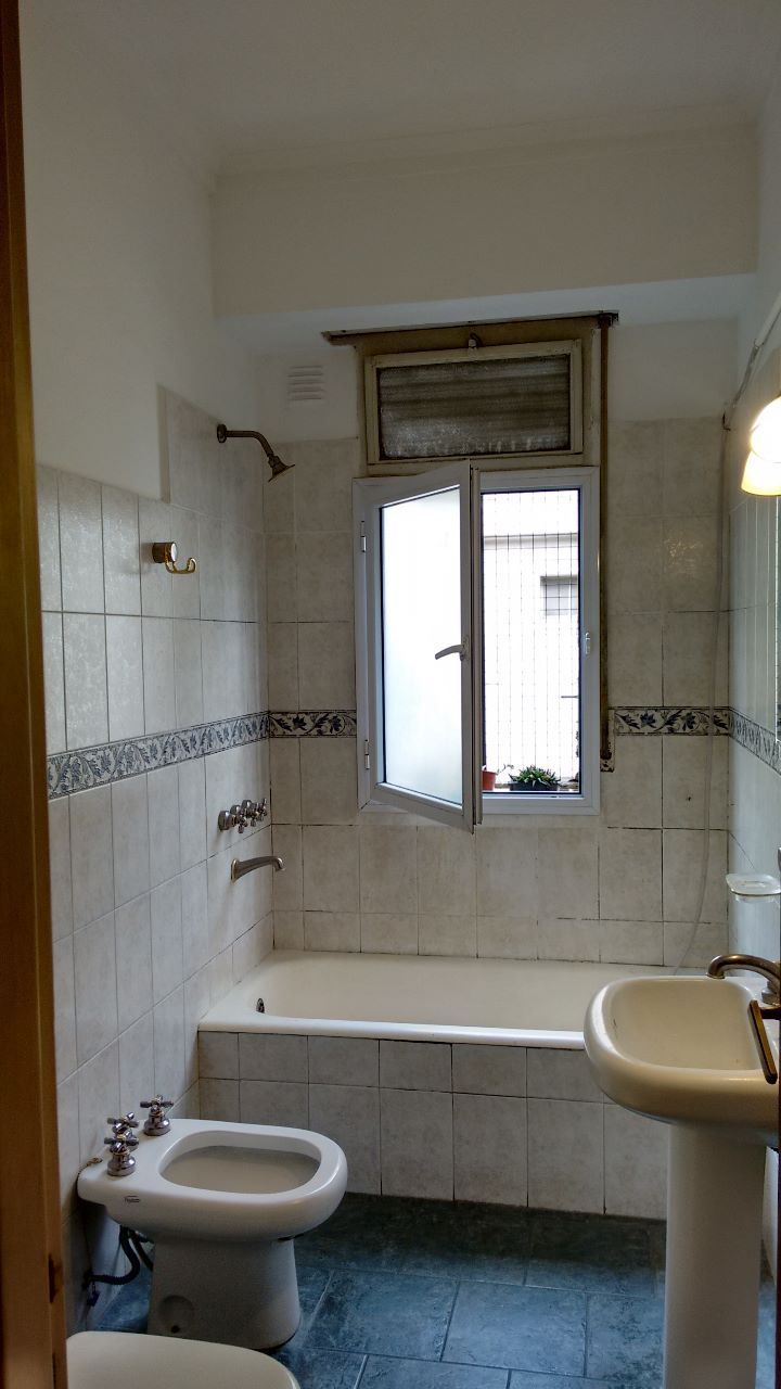 Baño pequeño con inodoro, lavabo, bañera, paredes alicatadas y una ventana encima de la bañera