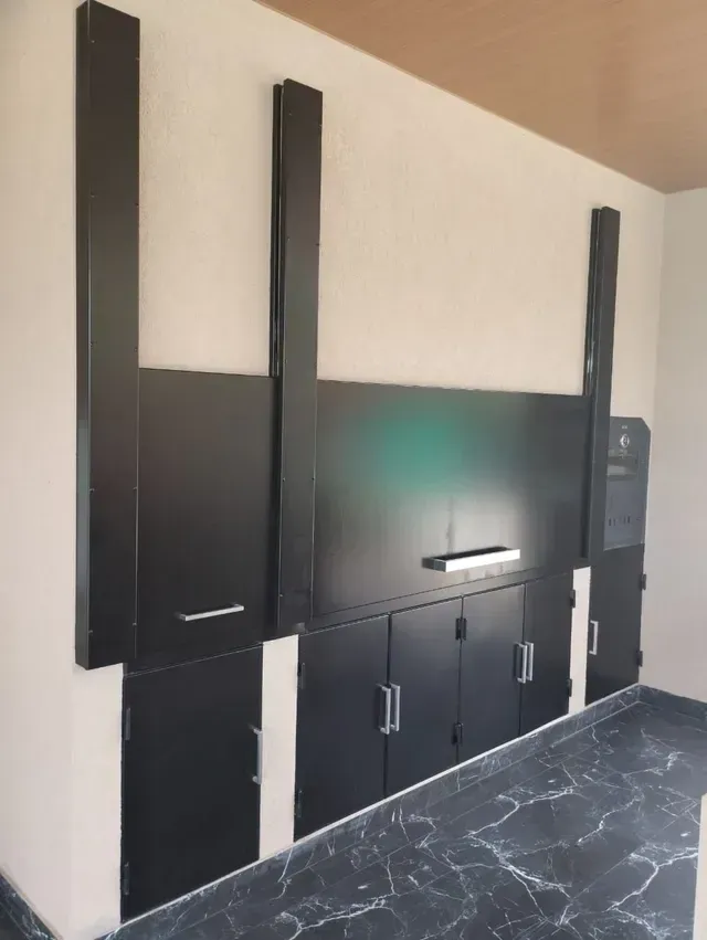 Armarios y estantes negros montados en la pared, sobre un suelo de mármol oscuro y frente a una pared beige.