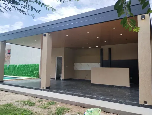 Entrada moderna cubierta con columnas beige, suelo de baldosas oscuras y mostrador de recepción bajo un techo inclinado