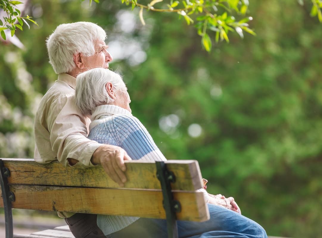 An elderly couple is sitting on a park bench.