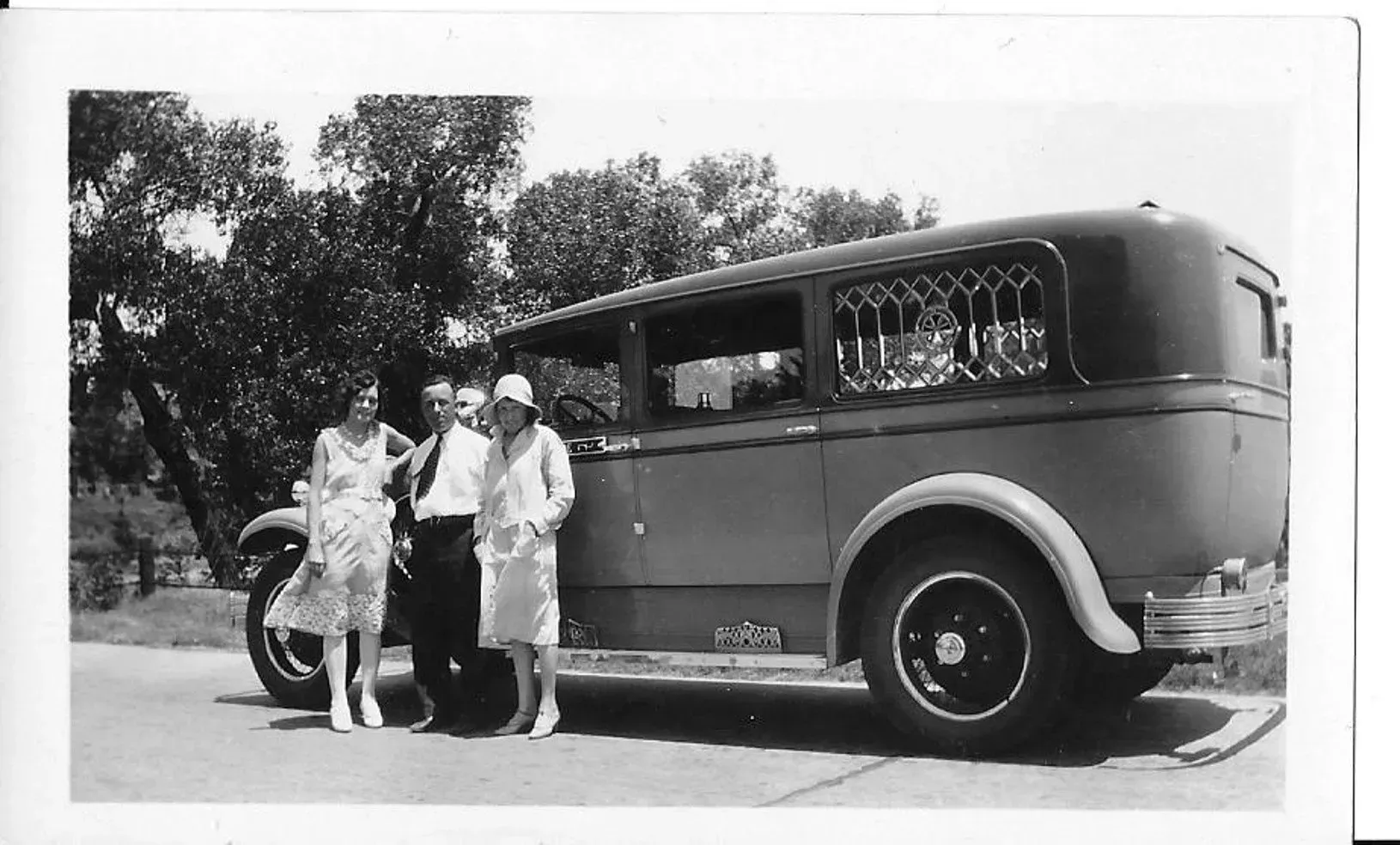 Three people stand beside a vintage bus parked on a sunny street.