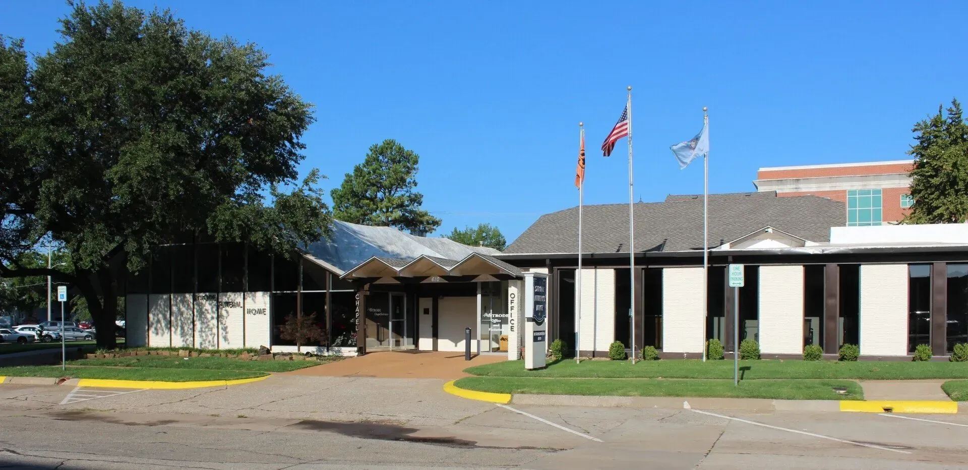 Single-story brick building with flags, trees, and a covered entrance on a sunny day