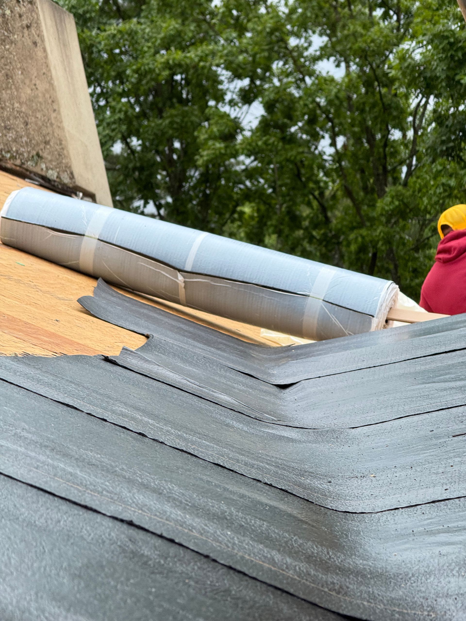 A person is laying a roll of roofing material on top of a roof.