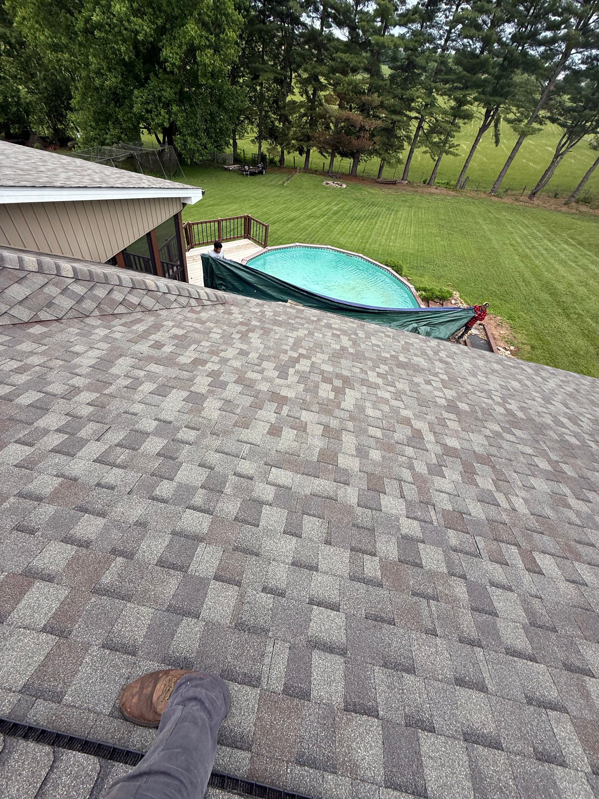 A person is standing on the roof of a house with a pool in the background.