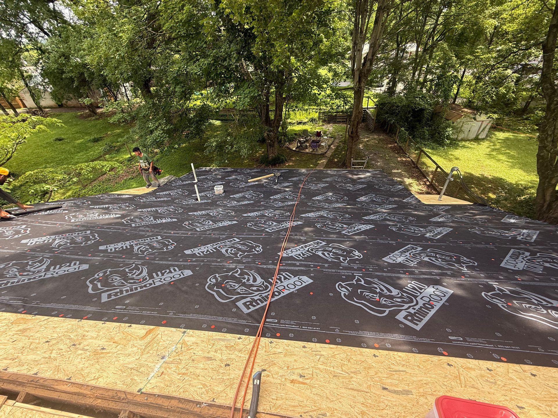 A roof is being installed in a backyard with trees in the background.
