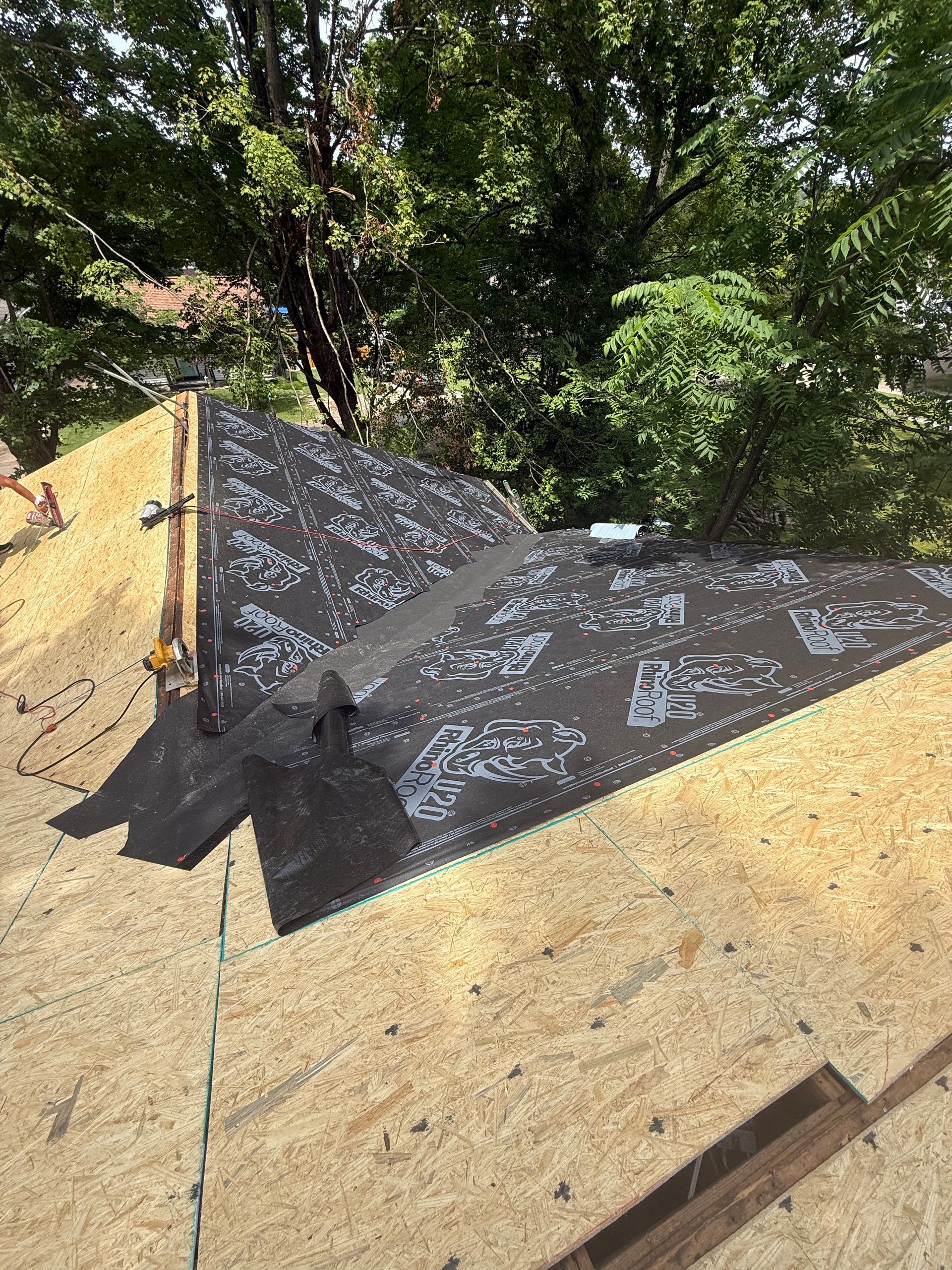 A roof is being installed on a house with trees in the background.