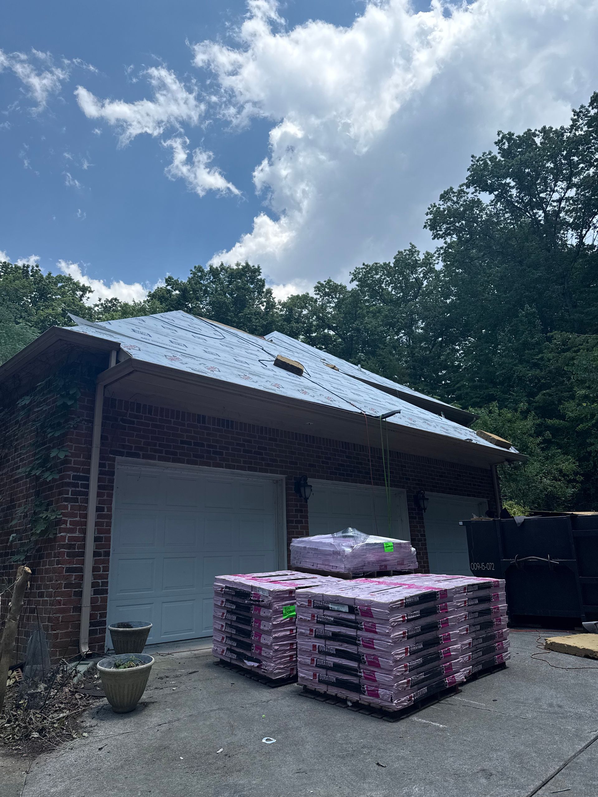 A brick garage with a blue roof and a bunch of pallets in front of it.
