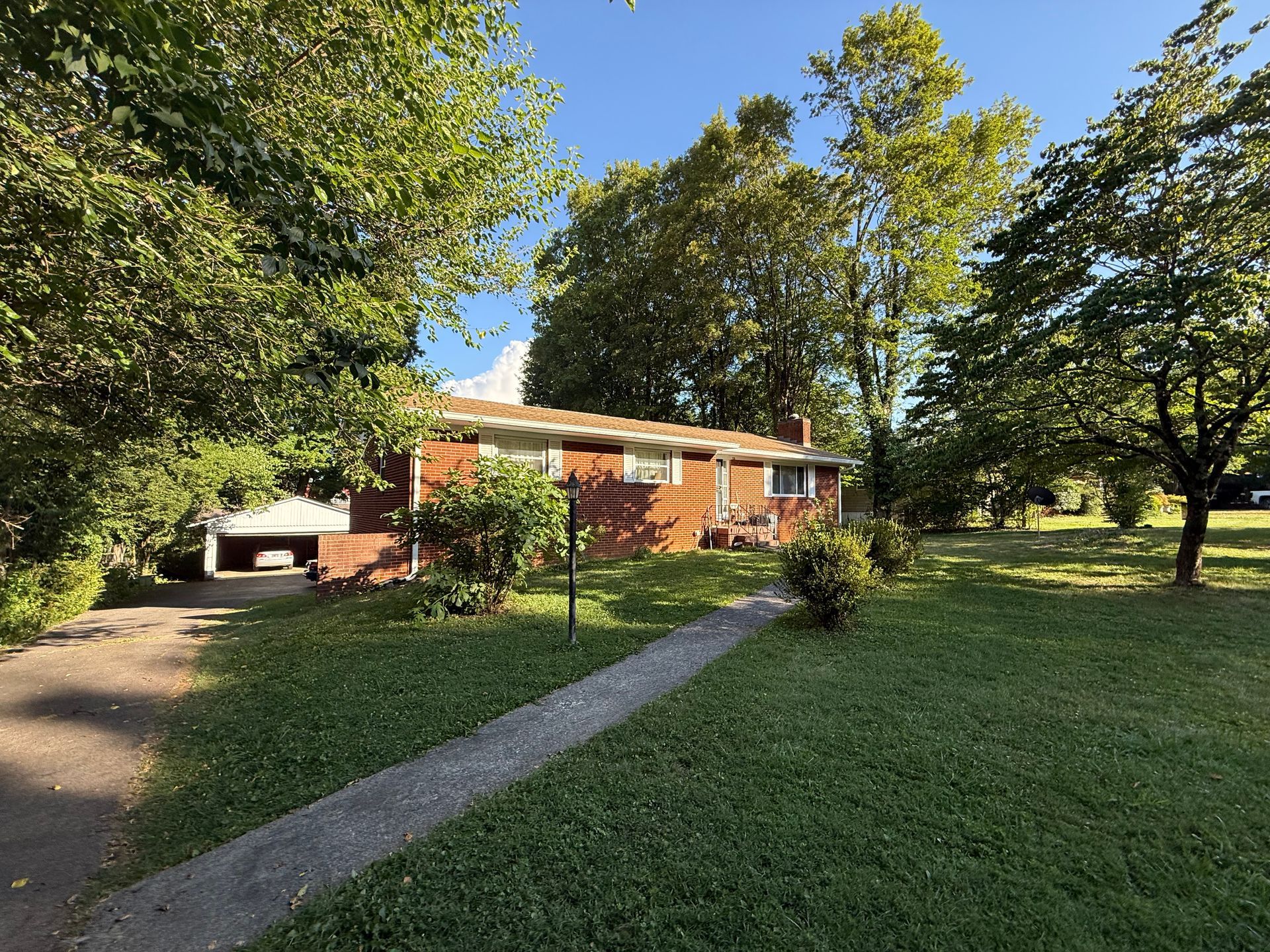A brick house with a driveway leading to it is surrounded by trees and grass.