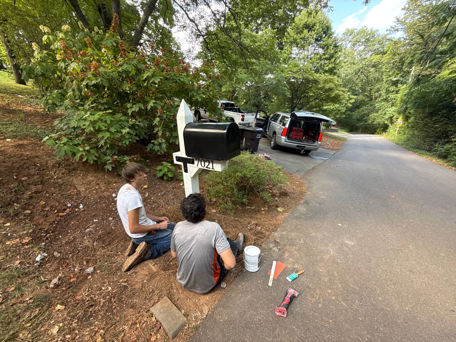 Two men are sitting on the side of the road next to a mailbox.