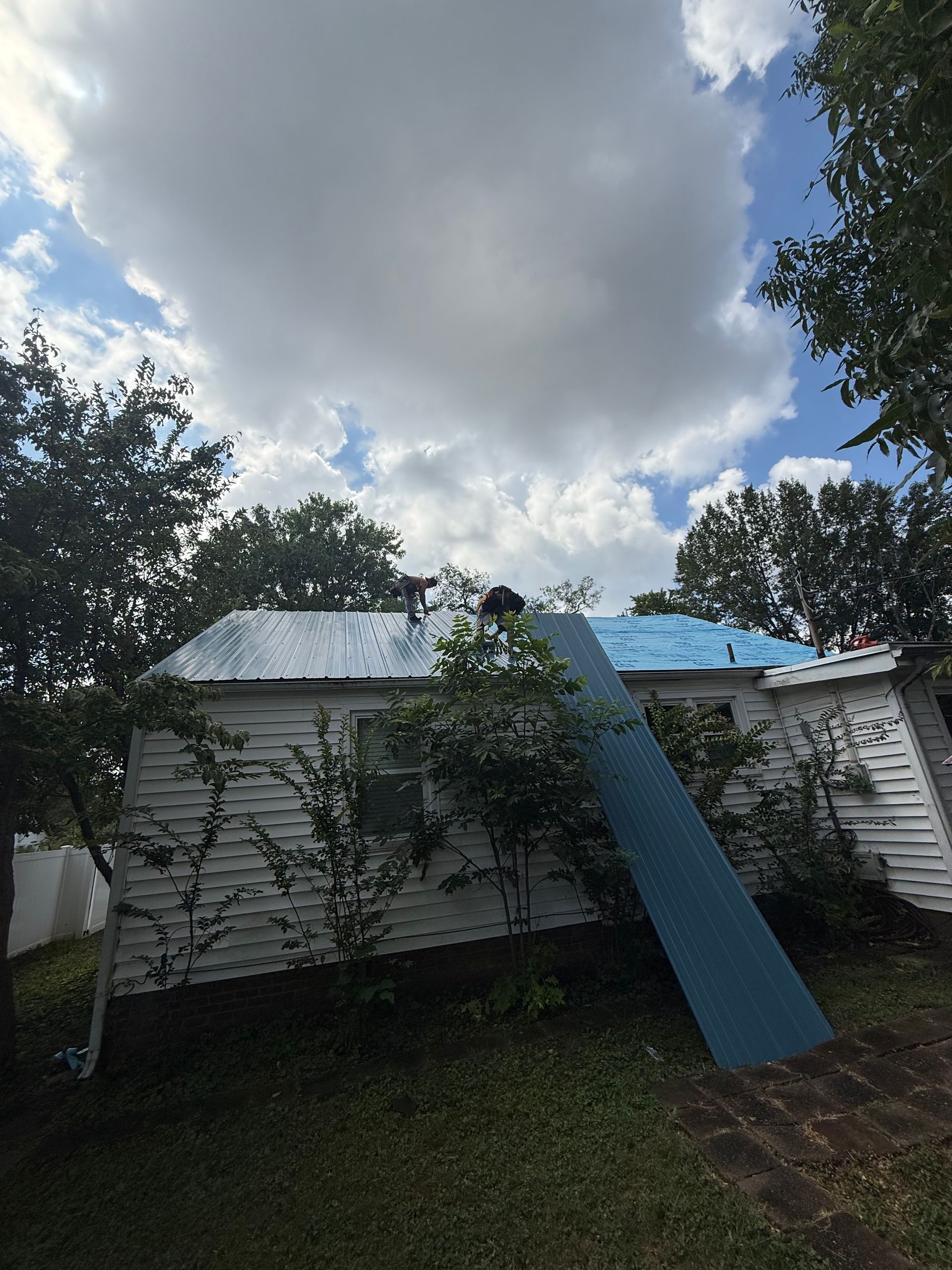 A white house with a blue tarp on the roof.