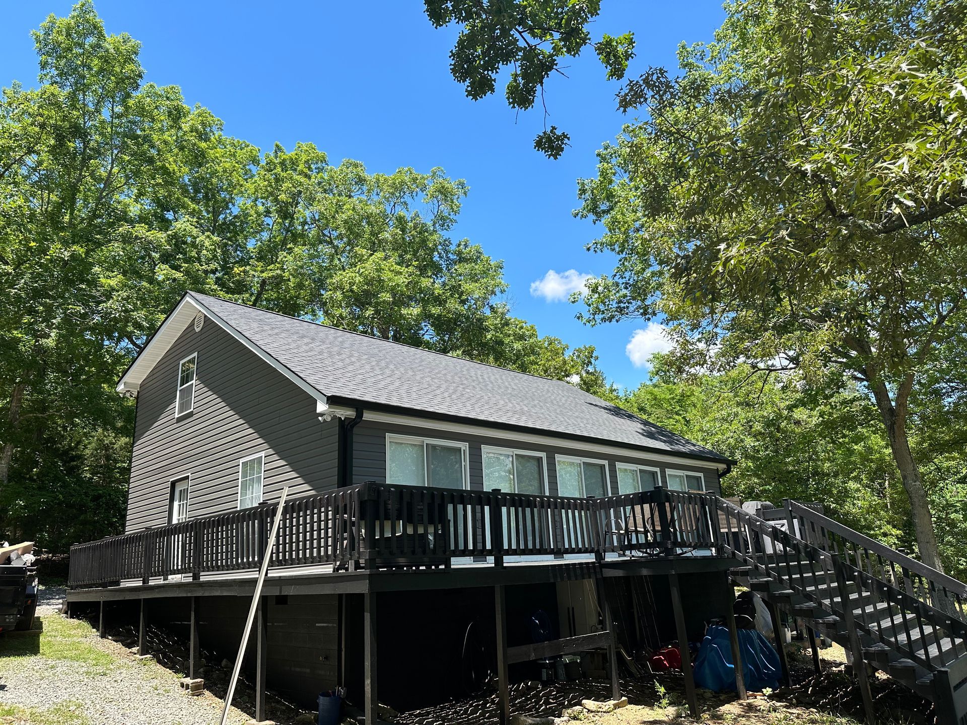A house with a large deck is surrounded by trees on a sunny day.