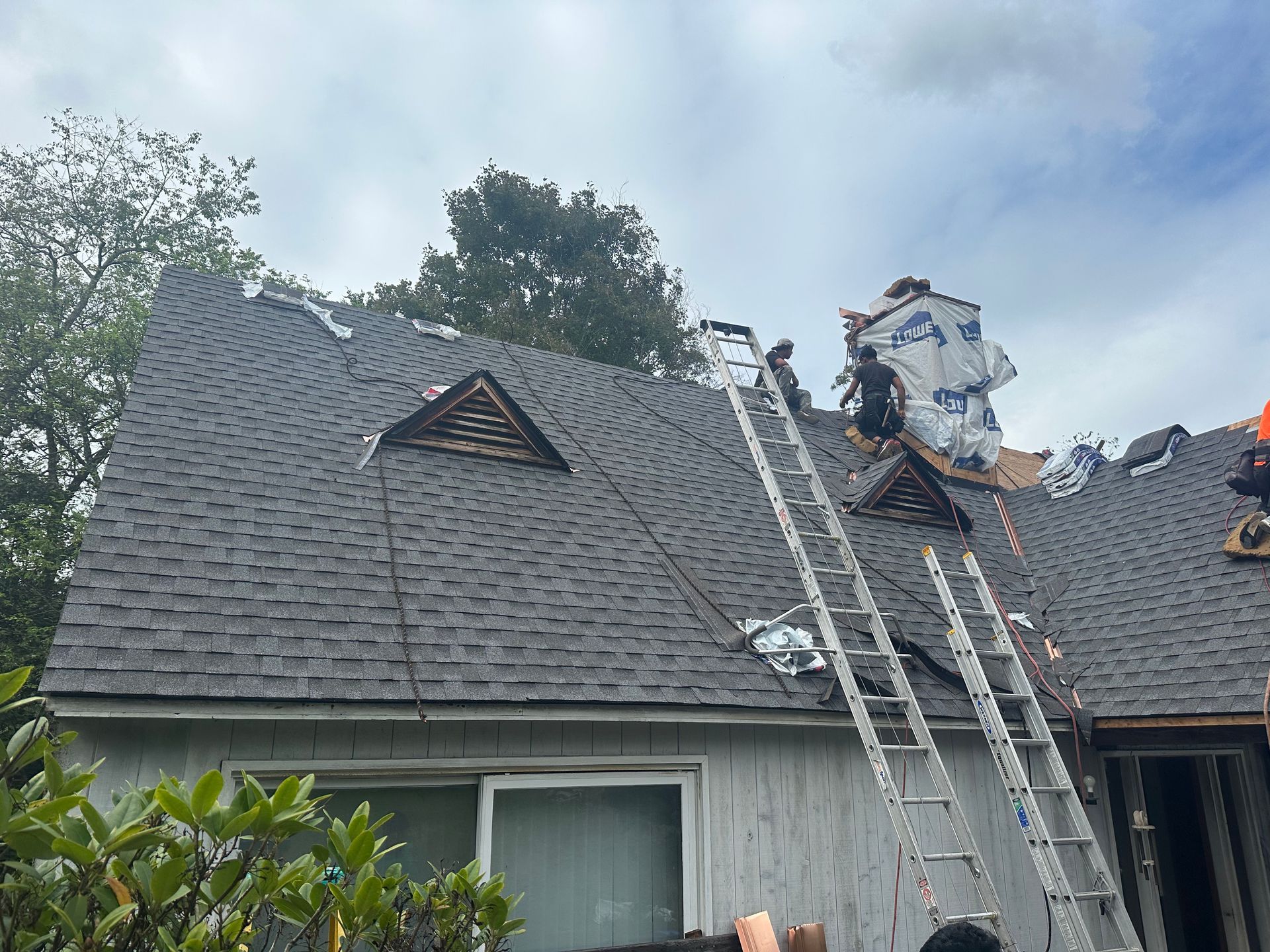 A man on a ladder is working on the roof of a house.