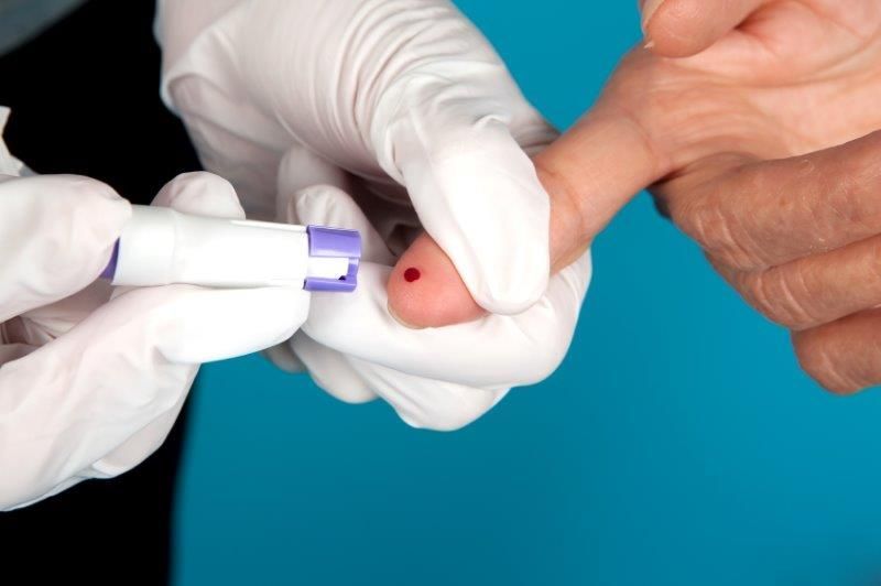 Gloved hand using a lancing device to draw blood from a patient’s fingertip