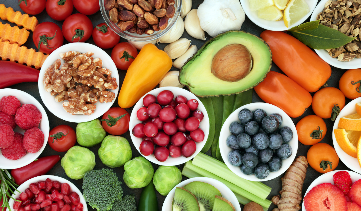Colourful assortment of fresh fruits and vegetables, including berries, avocado, citrus, and peppers on a white background