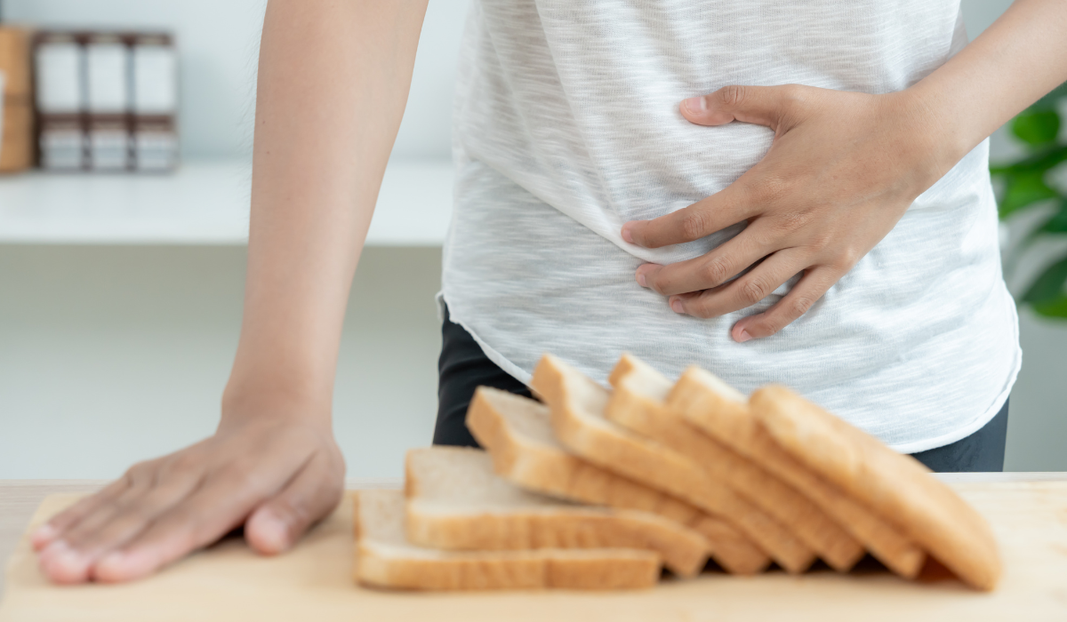 Person holding stomach beside a stack of sliced bread on a kitchen counter