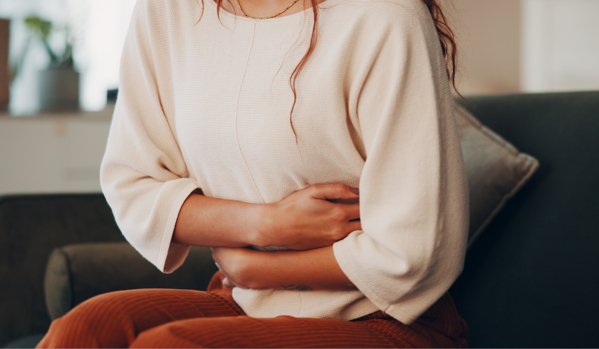 Person holding their stomach while sitting on a couch, suggesting abdominal pain