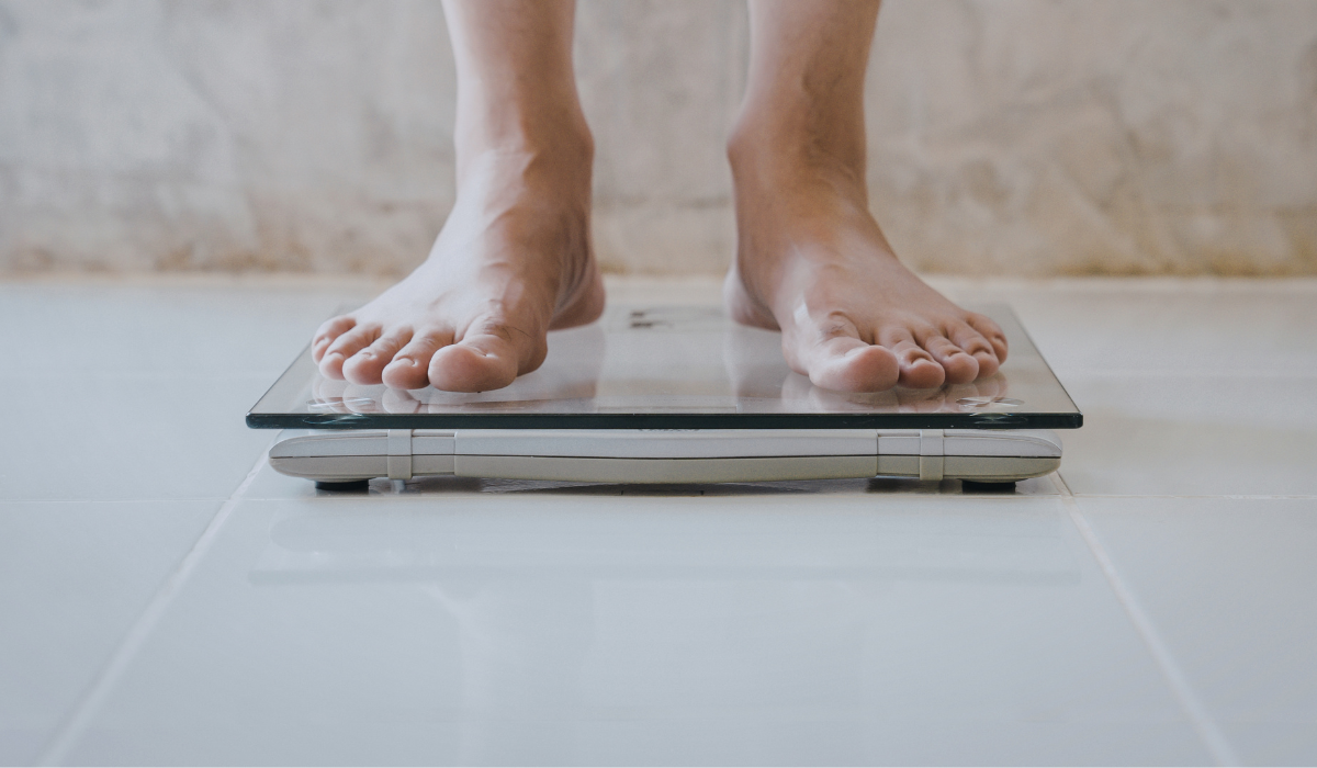 Bare feet standing on a glass bathroom scale on a tiled floor