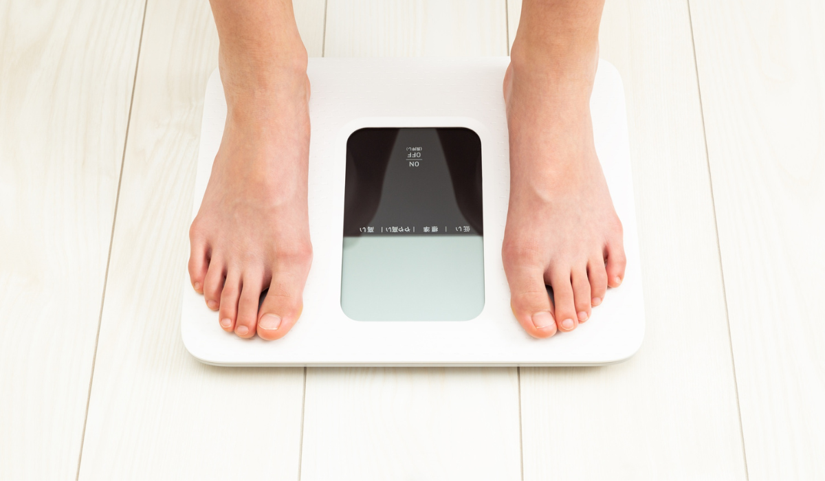 Feet on a white digital bathroom scale on a light wooden floor.