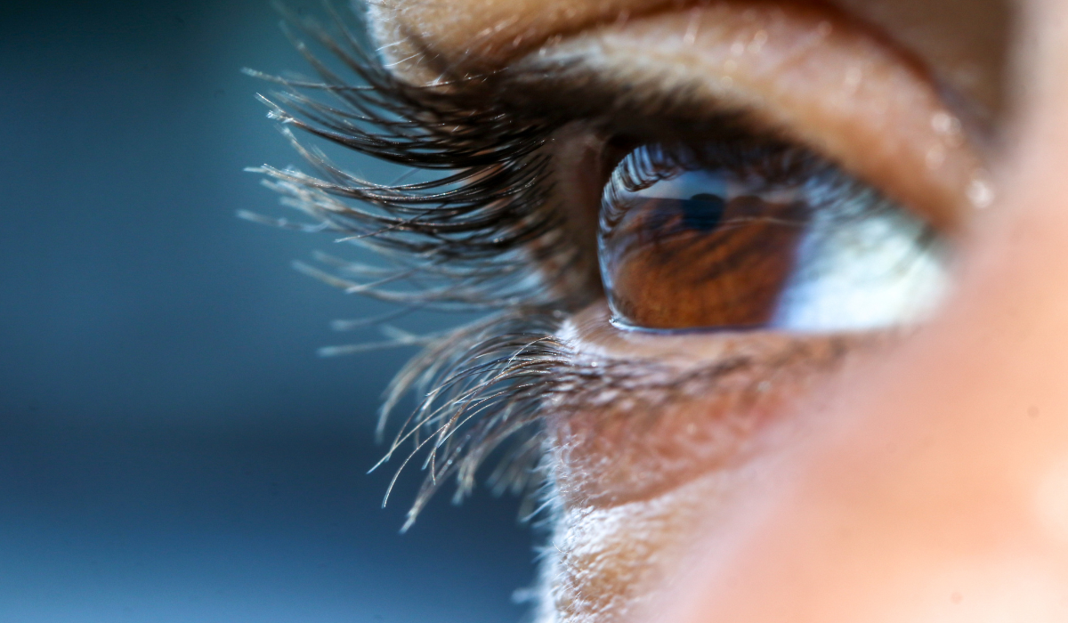 Close-up of a brown eye with long eyelashes against a blue background