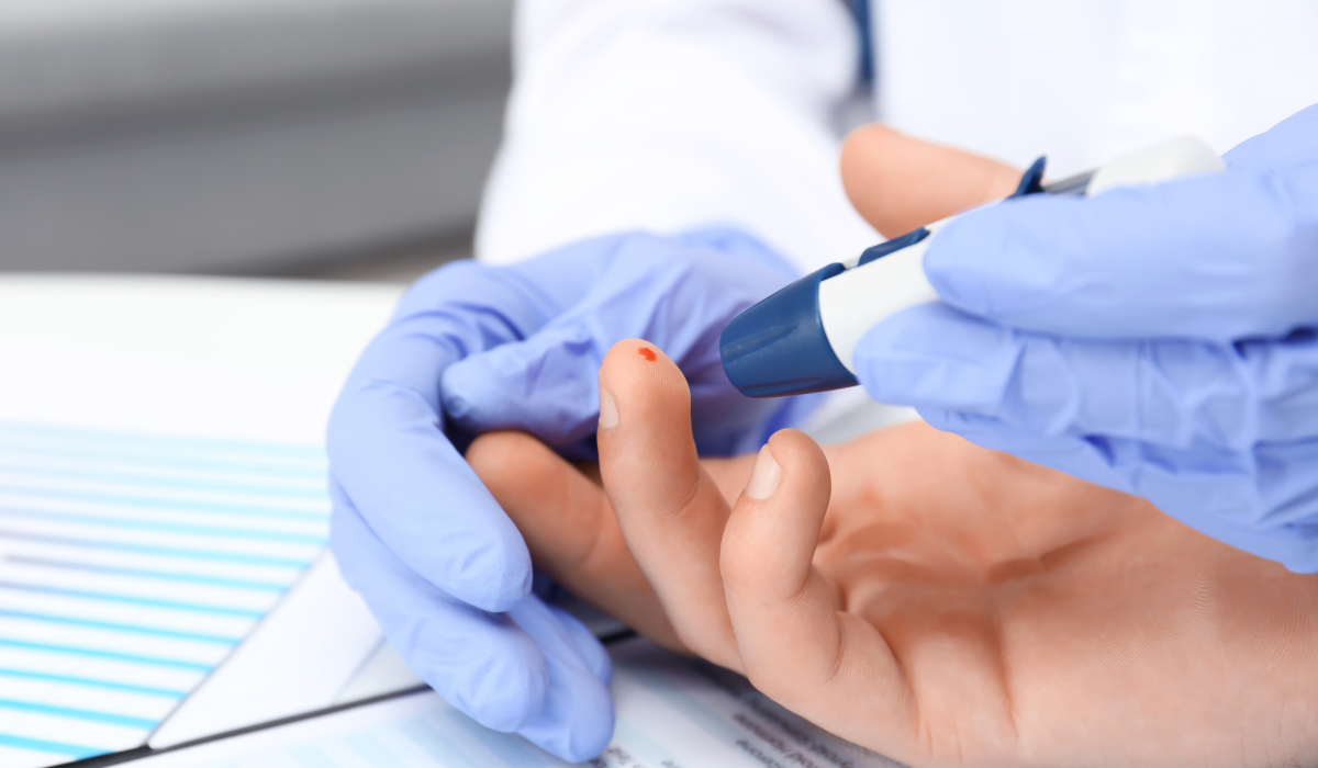Gloved hand using a lancing device to draw blood from a patient’s fingertip