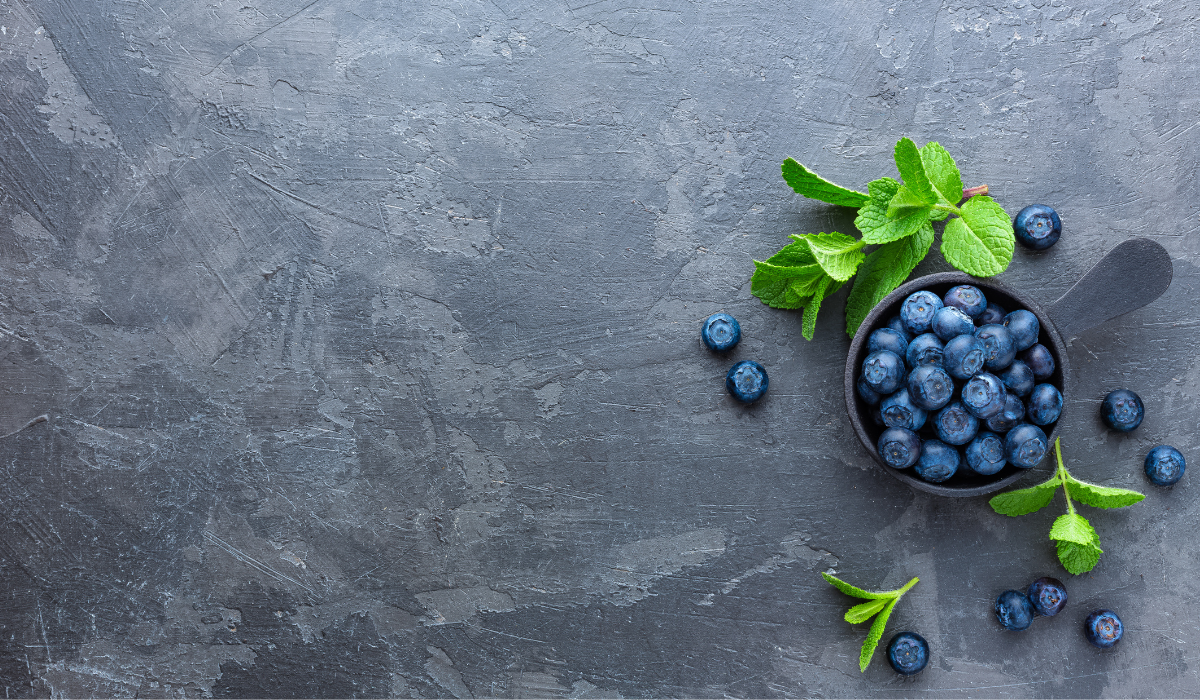 Blueberries and mint leaves in a black bowl on a dark stone surface