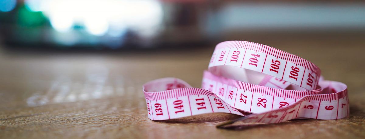 Pink measuring tape coiled on a wooden surface with a blurred background