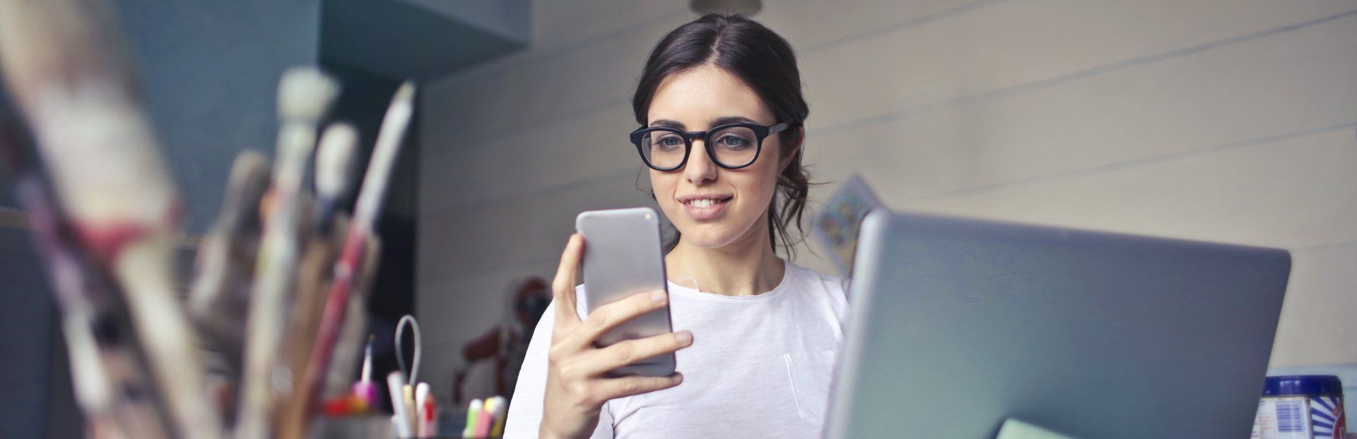 une femme est assise à un bureau et utilise un ordinateur portable et un téléphone portable.