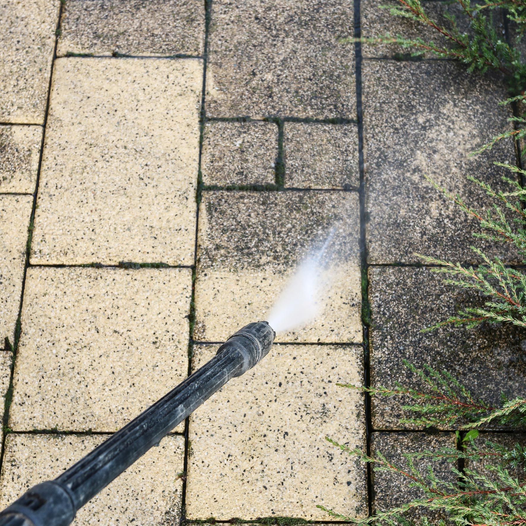 An unrecognized person is pressure washing brick pavers outside a residential home. An unrecognized person is pressure washing brick pavers outside a residential home.