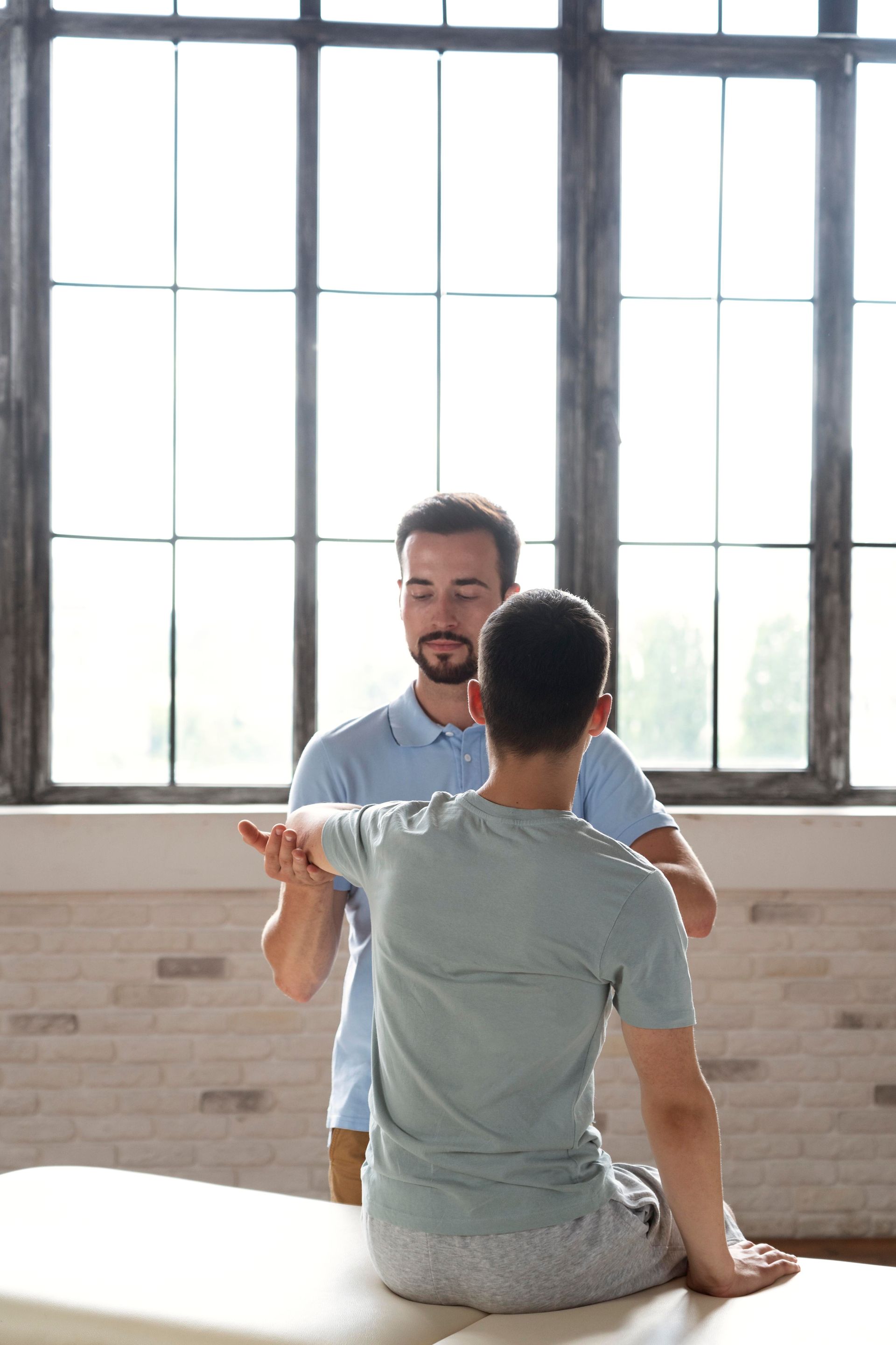Terapia ppstural a Moma Clinic Andorra. Un hombre está sentado en una mesa haciendo terapia postural con otro hombre.