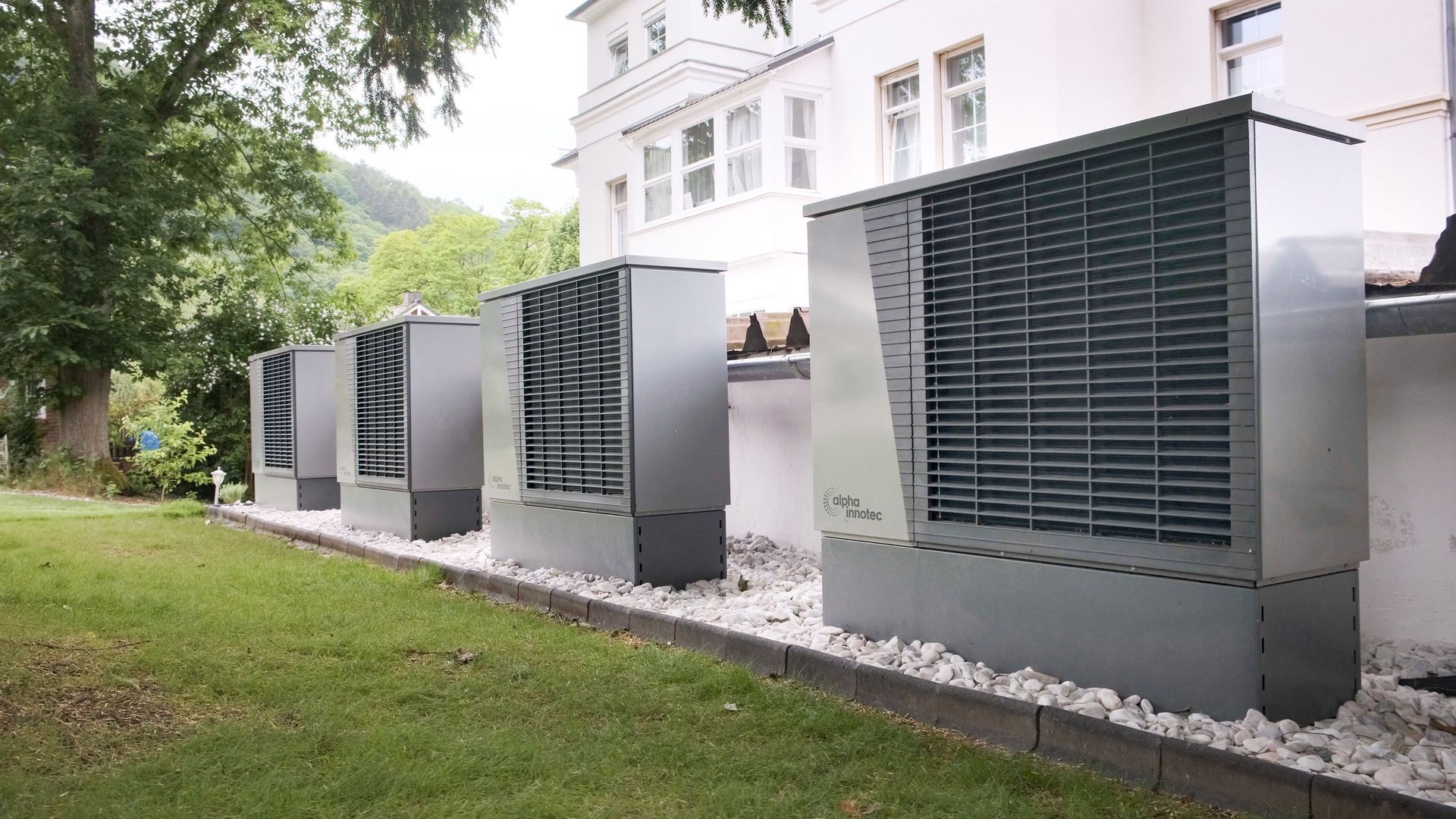 Row of large gray outdoor HVAC units beside a white building on a grassy lawn