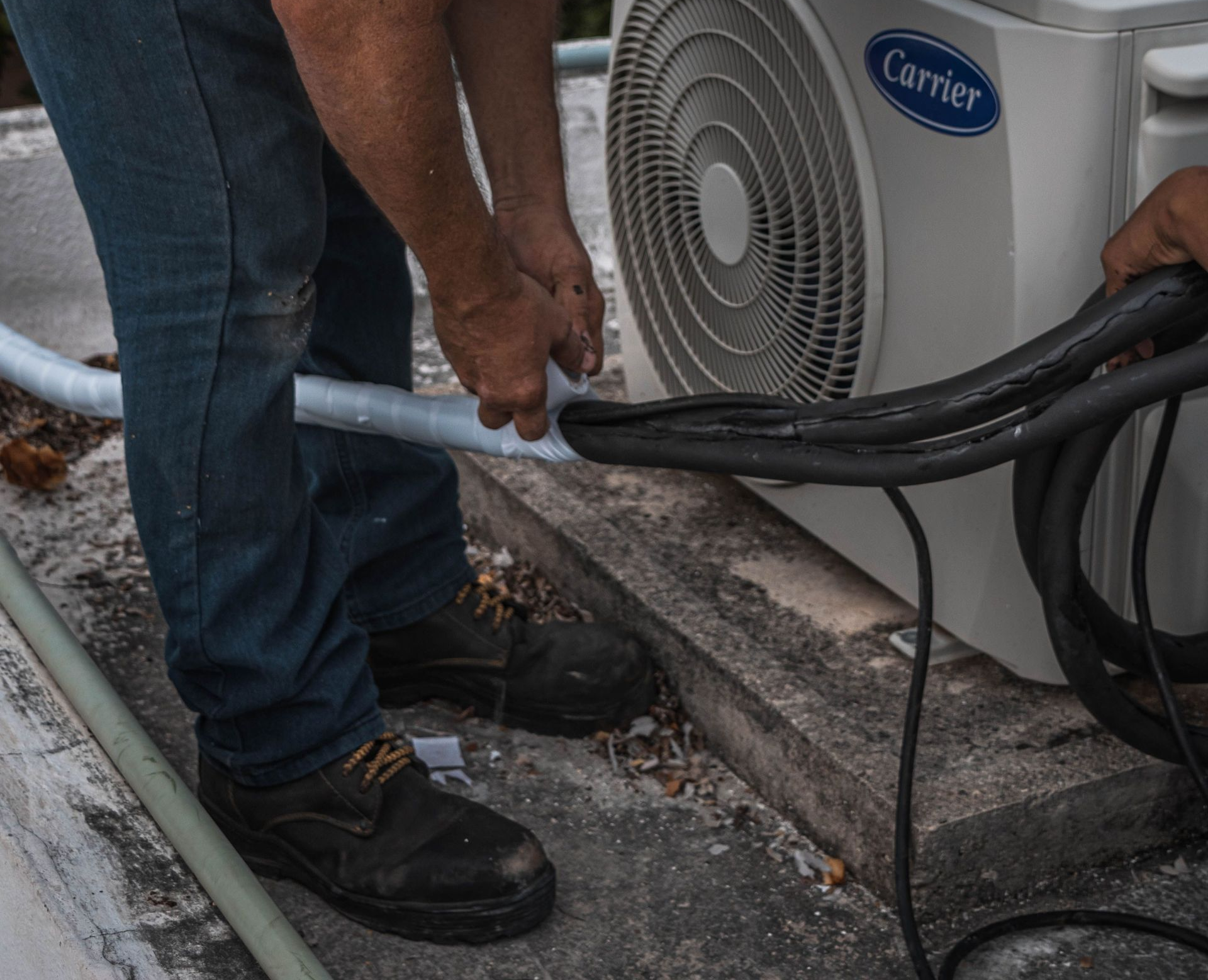 Technician connecting insulated copper pipes to a Carrier outdoor air conditioner unit