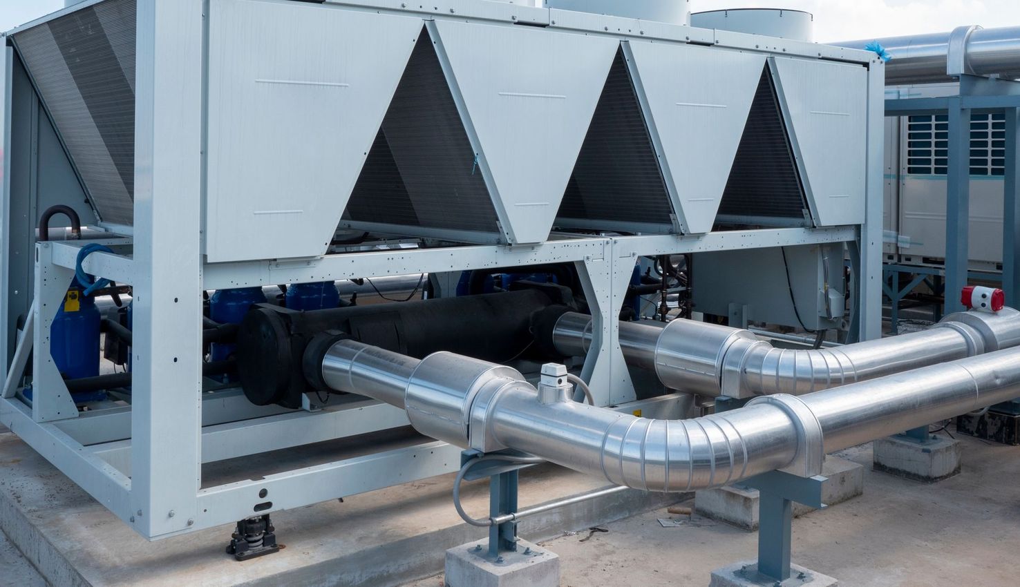 Industrial HVAC chiller units with silver ducting and piping outdoors on a rooftop platform
