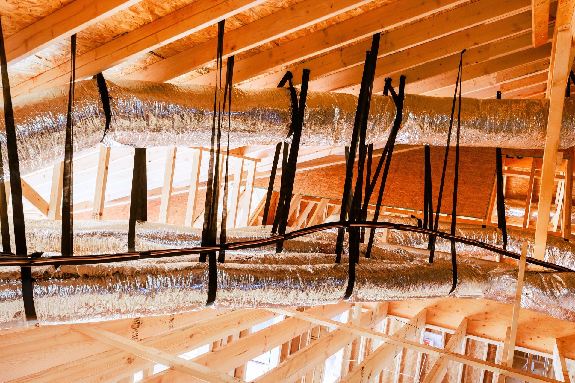 Exposed attic framing with wooden beams, insulation, and hanging black wires under a roof structure