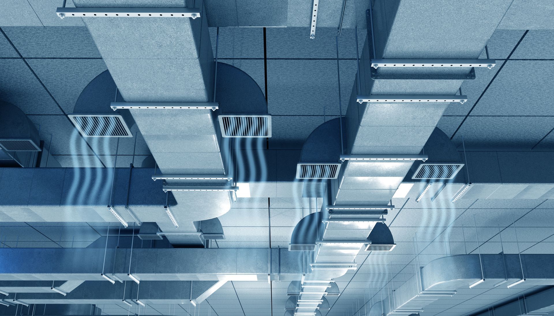 Blue-toned ceiling with exposed vents, fluorescent lights, and hanging cables in an industrial interior