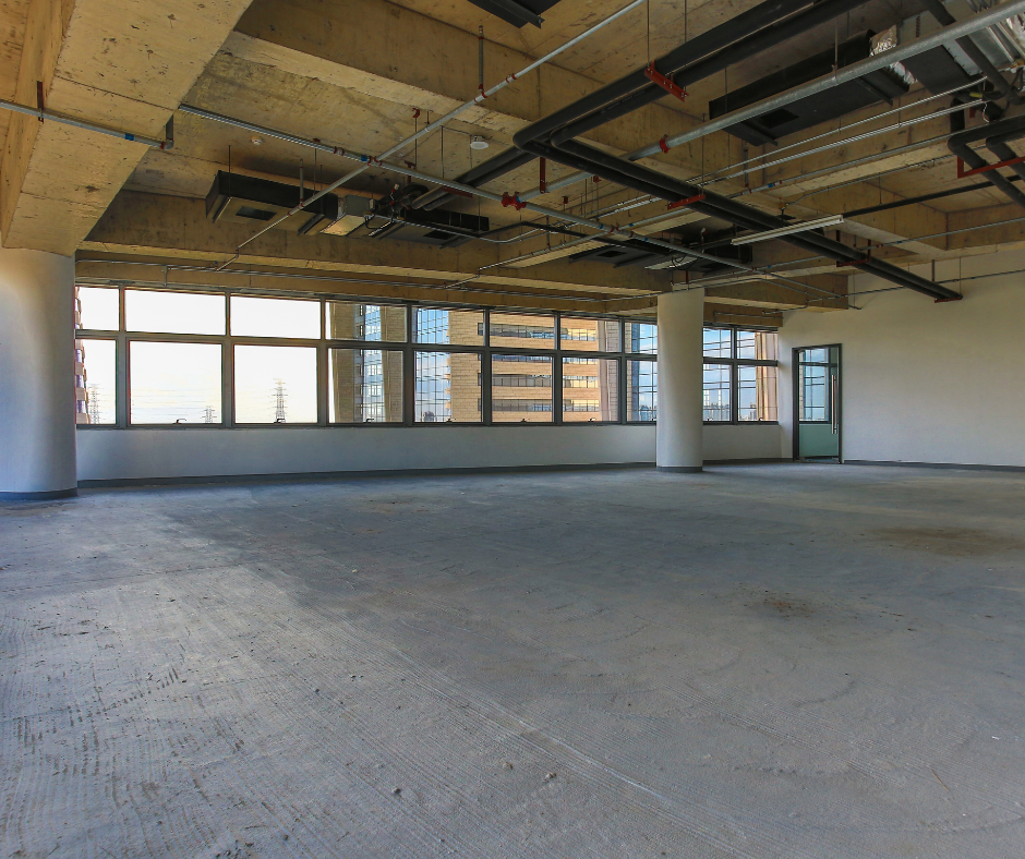 Empty office interior with exposed ceiling, concrete floor, and large windows