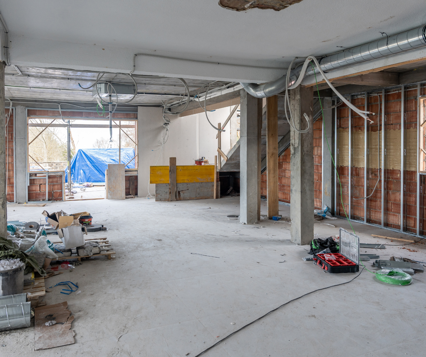 Interior of a gutted building under renovation, with exposed studs, debris, and unfinished concrete floors