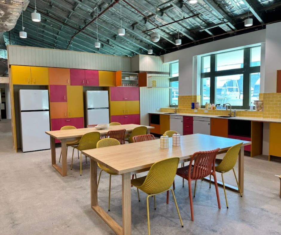 Modern communal kitchen with colorful cabinets, wooden tables, and a bright industrial ceiling