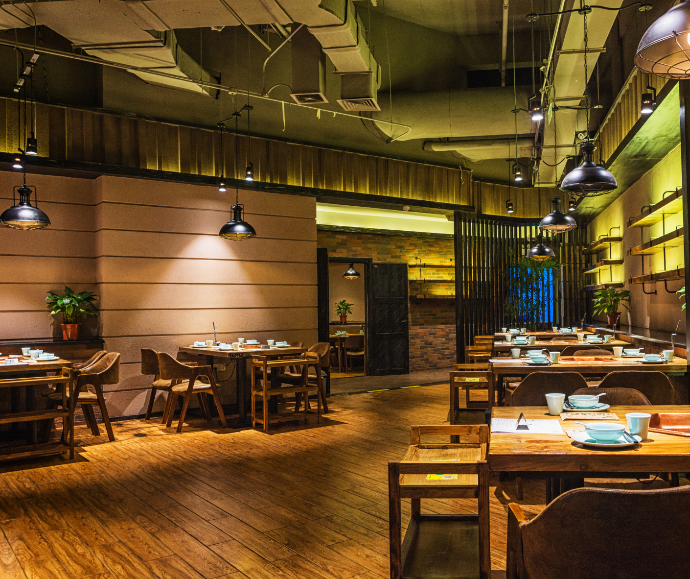 Warm, dimly lit restaurant interior with wooden tables, hanging lights, and exposed industrial ceiling.