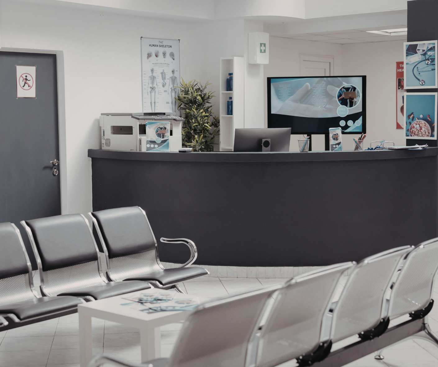 Empty clinic waiting room with gray chairs and a black reception desk in front