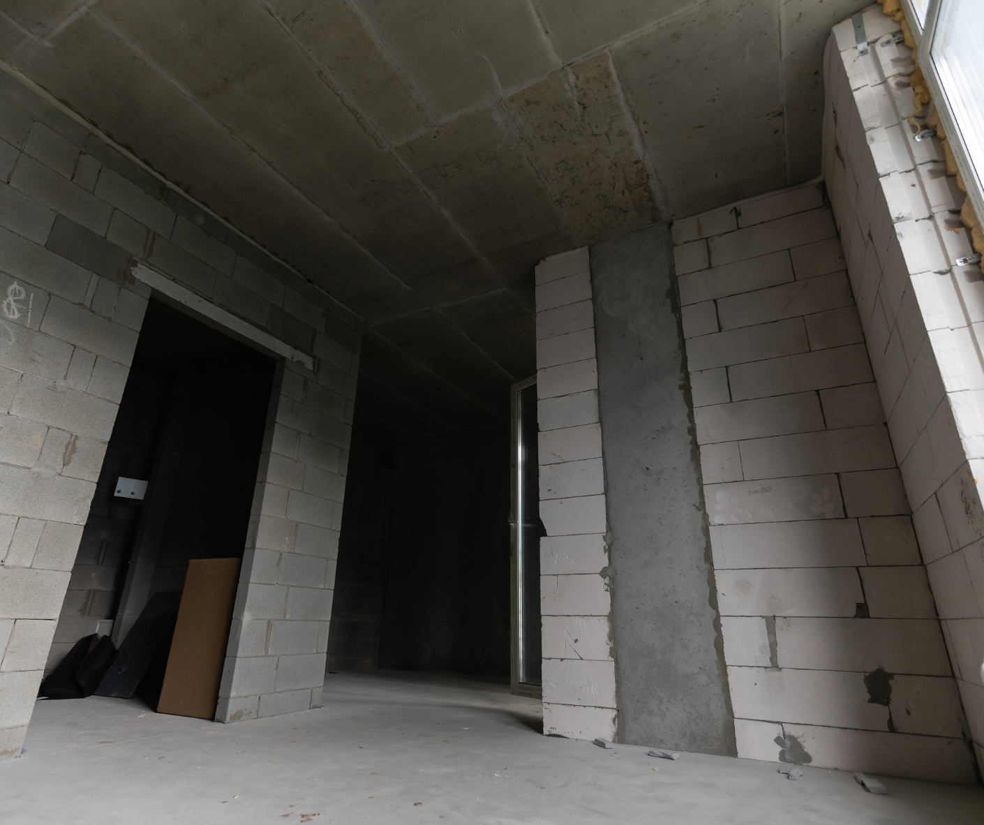 Unfinished concrete interior with open doorways, cinder block walls, and a stairwell opening on the right Unfinished concrete interior with open doorways, cinder block walls, and a stairwell opening on the right