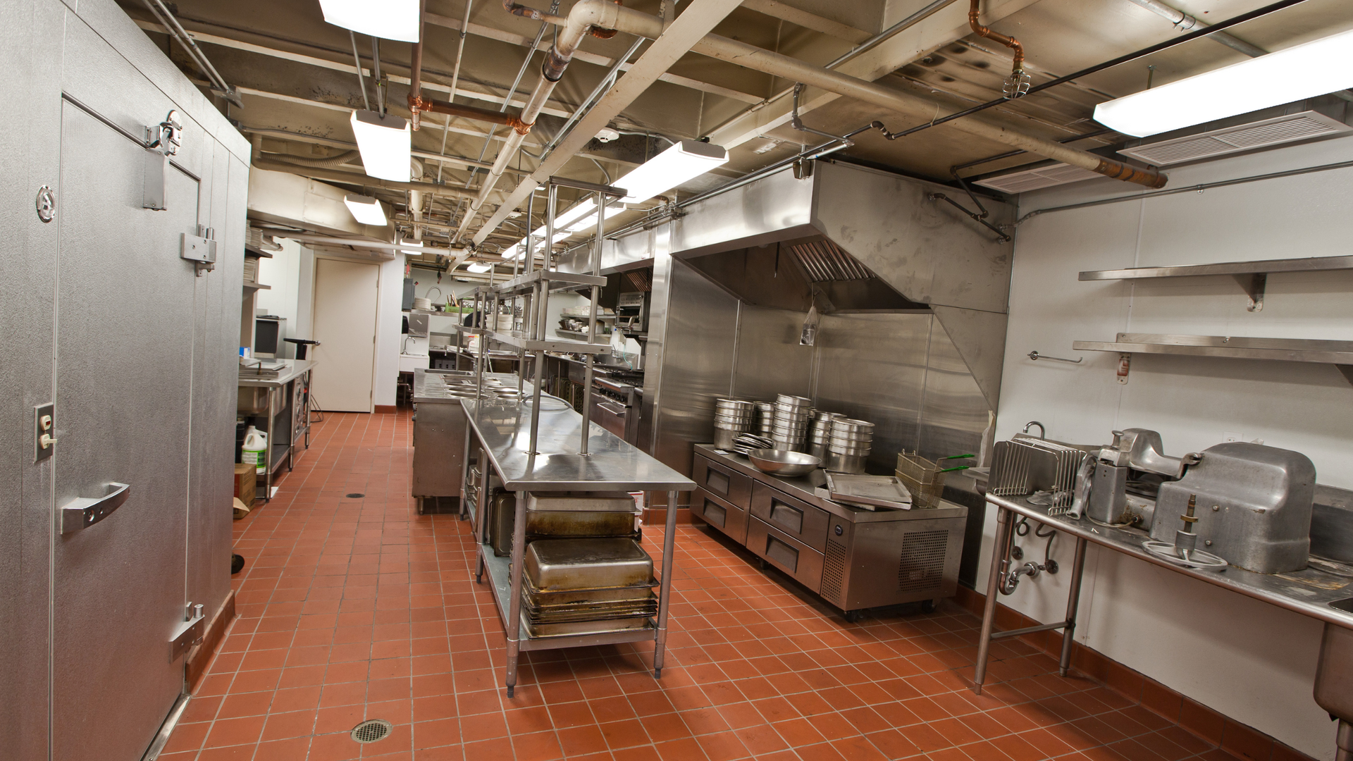 Large commercial kitchen with red tiled floor, stainless preparation benches and canopy range hood. Large commercial kitchen with red tiled floor, stainless preparation benches and canopy range hood.