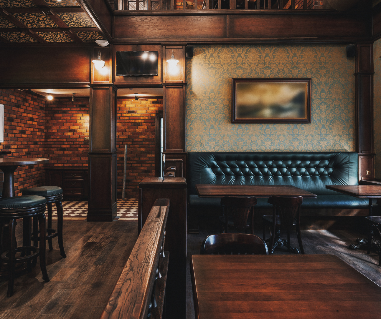 Empty rustic bar interior with brick walls, wooden tables, and tufted green banquette seating Empty rustic bar interior with brick walls, wooden tables, and tufted green banquette seating